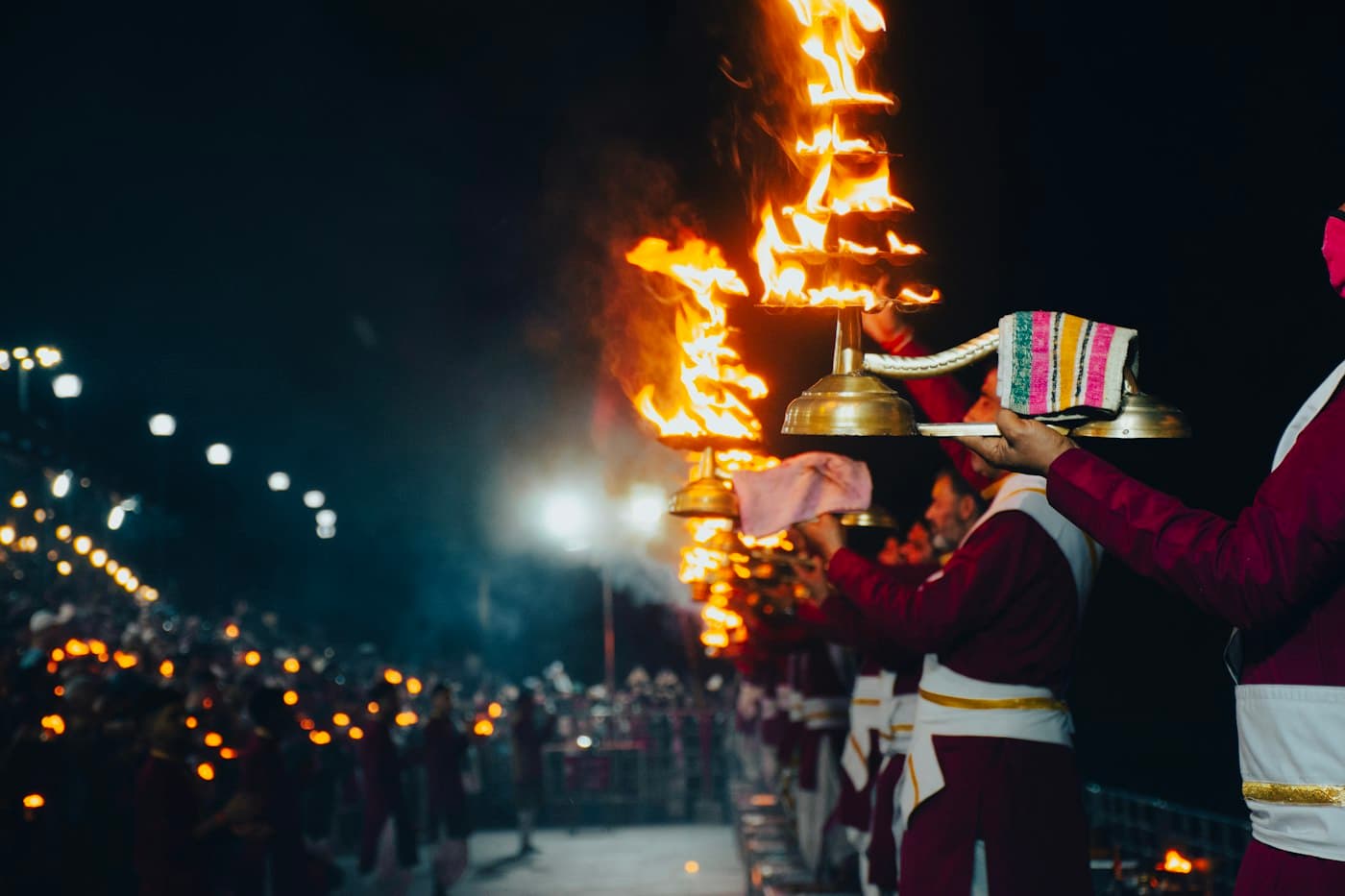 Priests in a line holding flaming aarti lamps at night