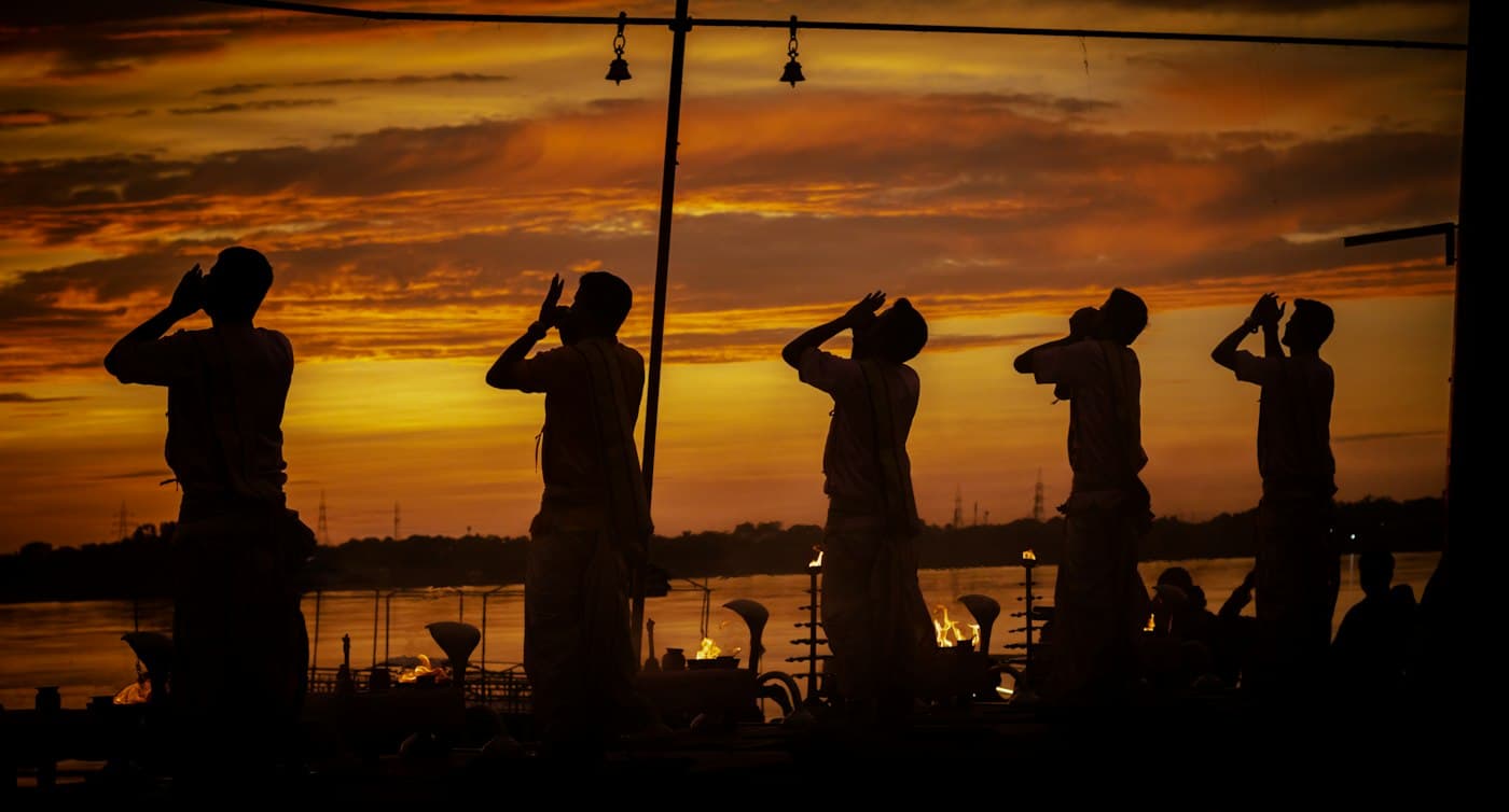 Silhouettes of devotees along the riverbank at twilight