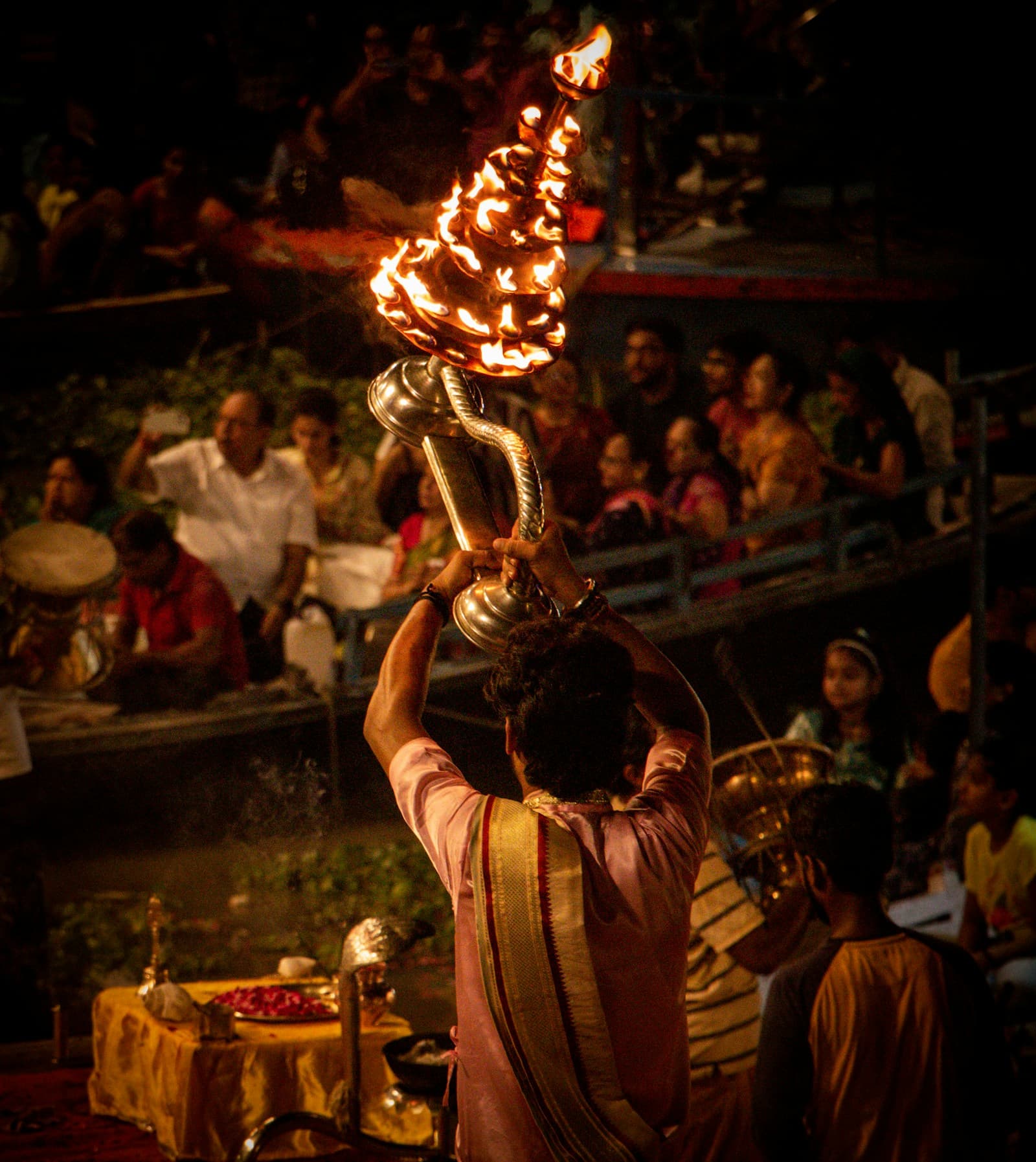 A priest raising a flaming aarti lamp before devotees during a cultural riverside ceremony in Kashi